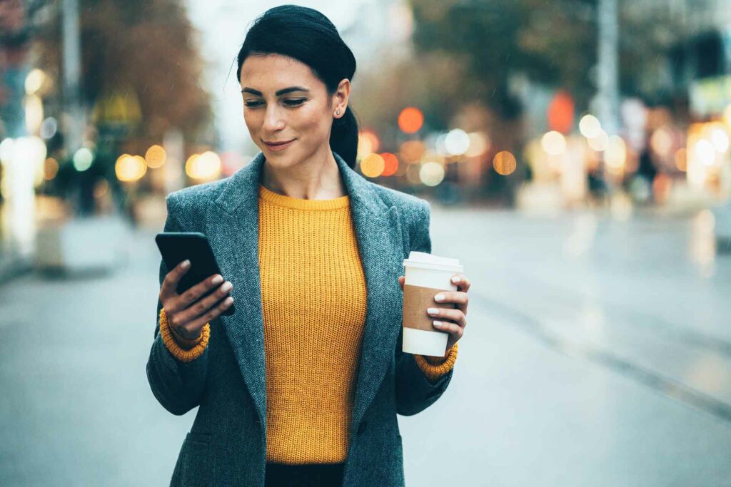 Mujer joven caminando por la calle, viendo su celular.