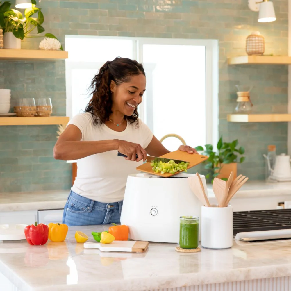 Una mujer utilizando un electrodoméstico ecológico, colocando verduras dentro.